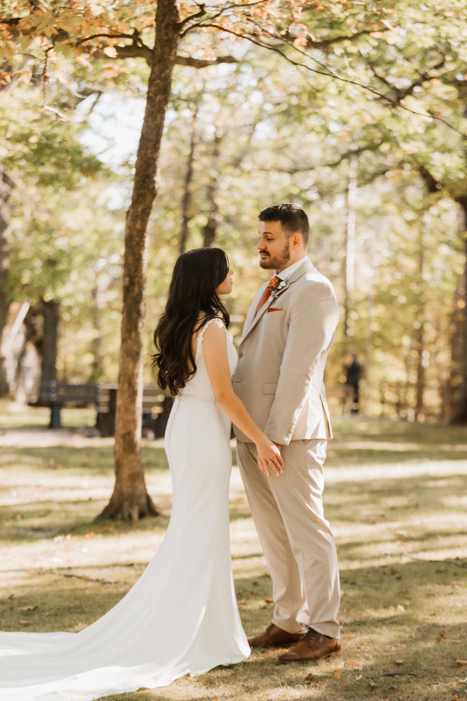 A couple shares a joyful moment together during their outdoor wedding photoshoot in a sunlit wooded setting.