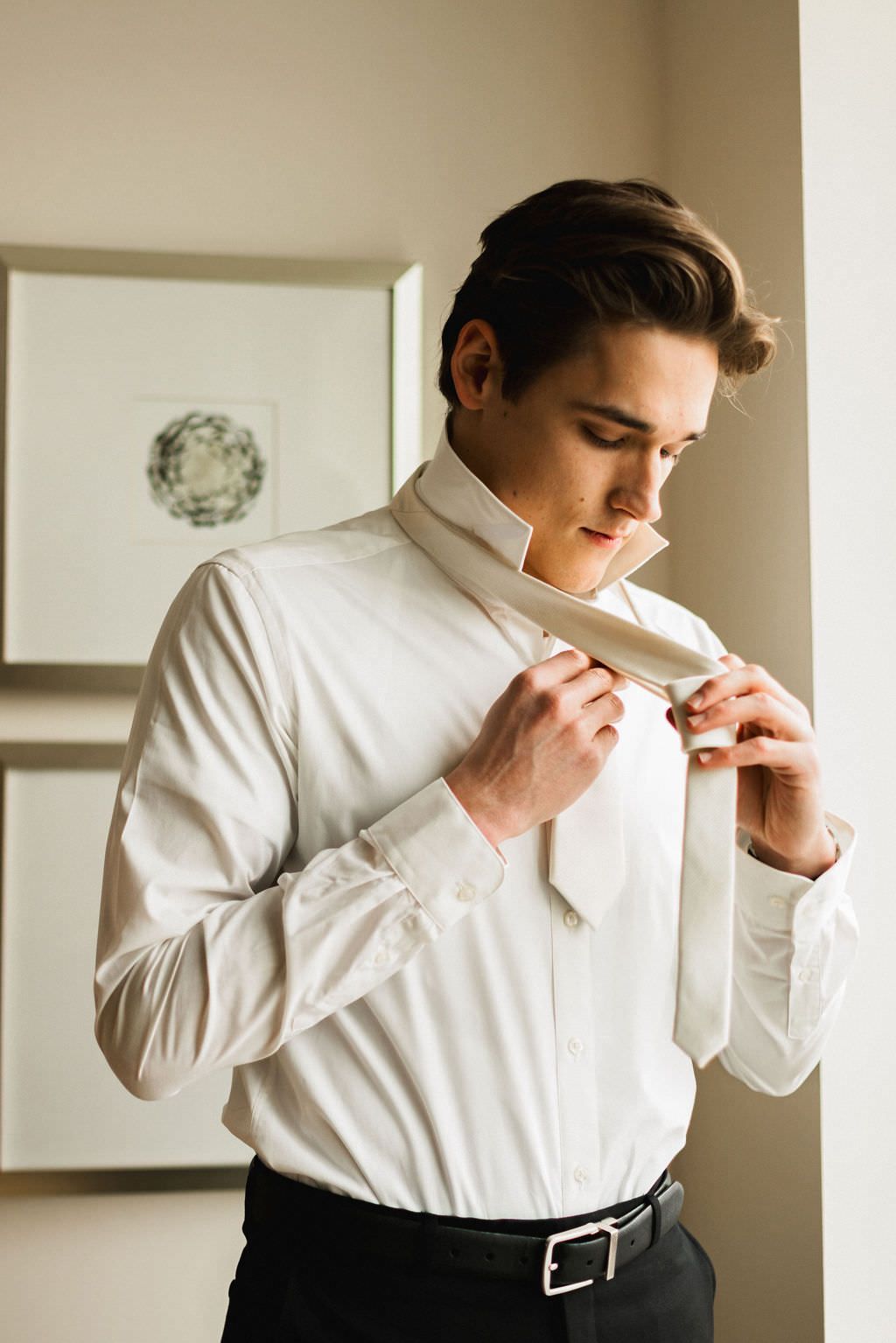 Groom adjusting his white dress shirt collar while getting ready for the wedding ceremony.