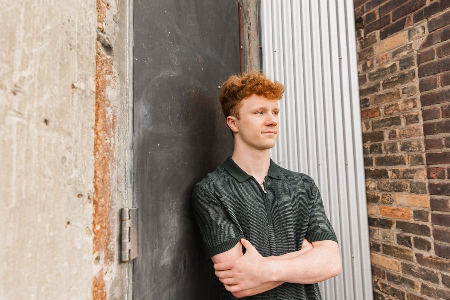 A person with red hair stands against weathered brick walls and white columns in an architectural setting.
