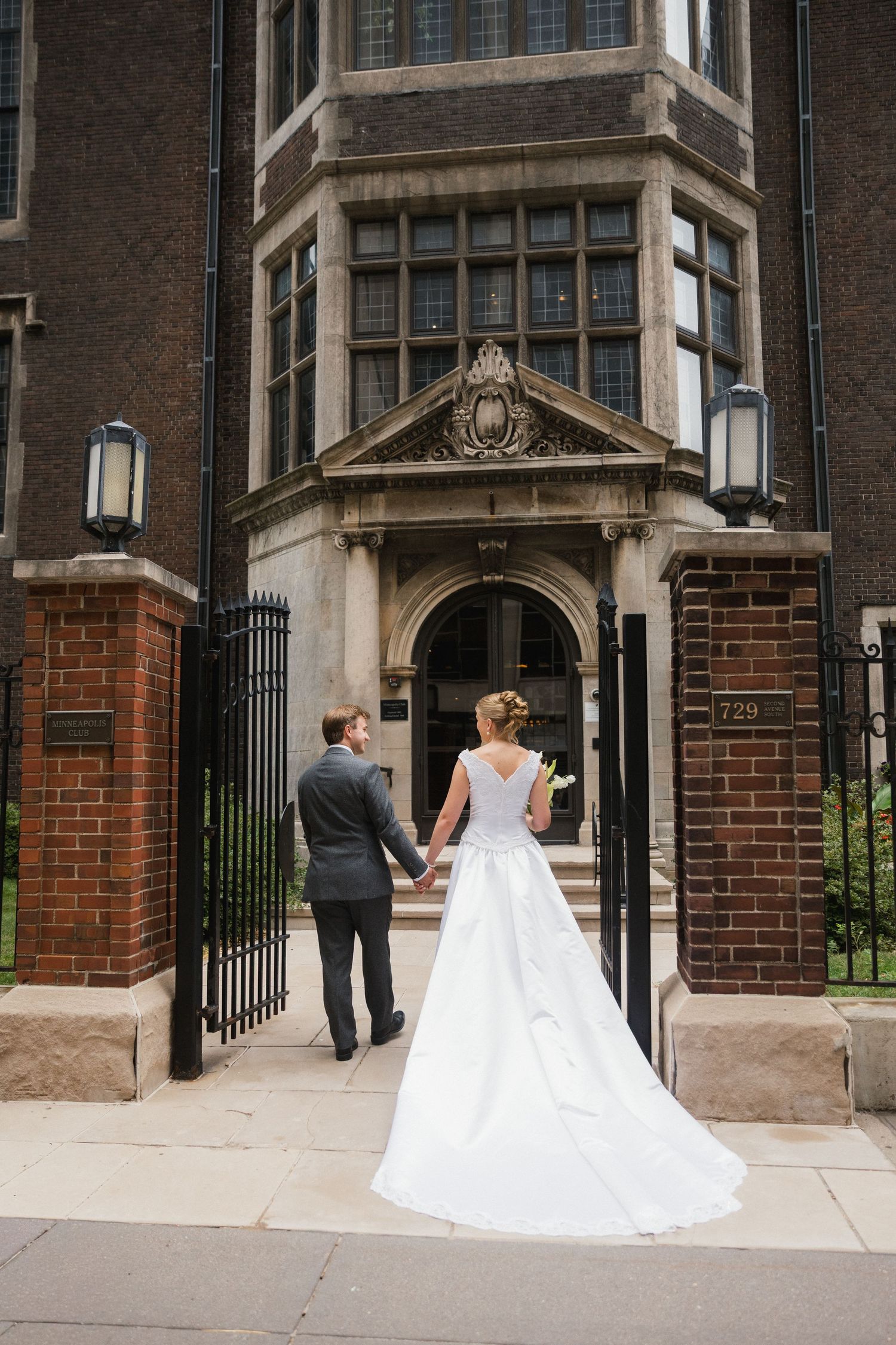 Bride and groom hold hands walking toward ornate brick building entrance on their wedding day.