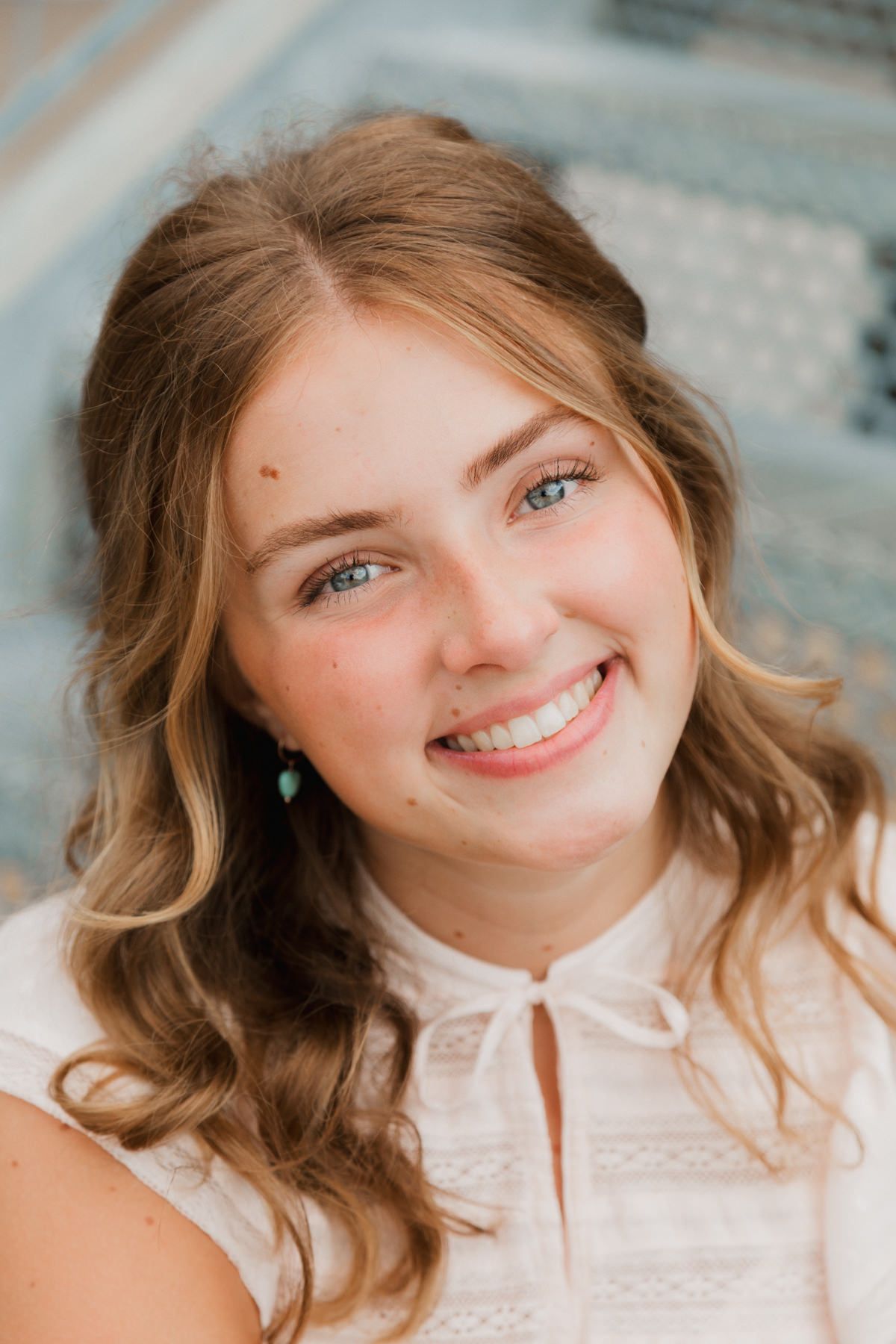 Close-up portrait of smiling teen girl with blue eyes and turquoise earrings outdoors.