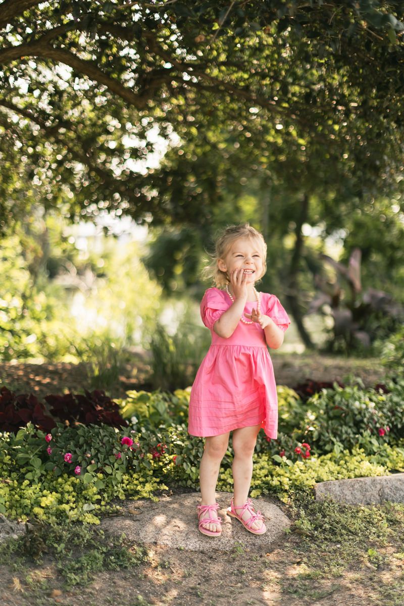 Toddler in pink dress exploring garden path on sunny day.