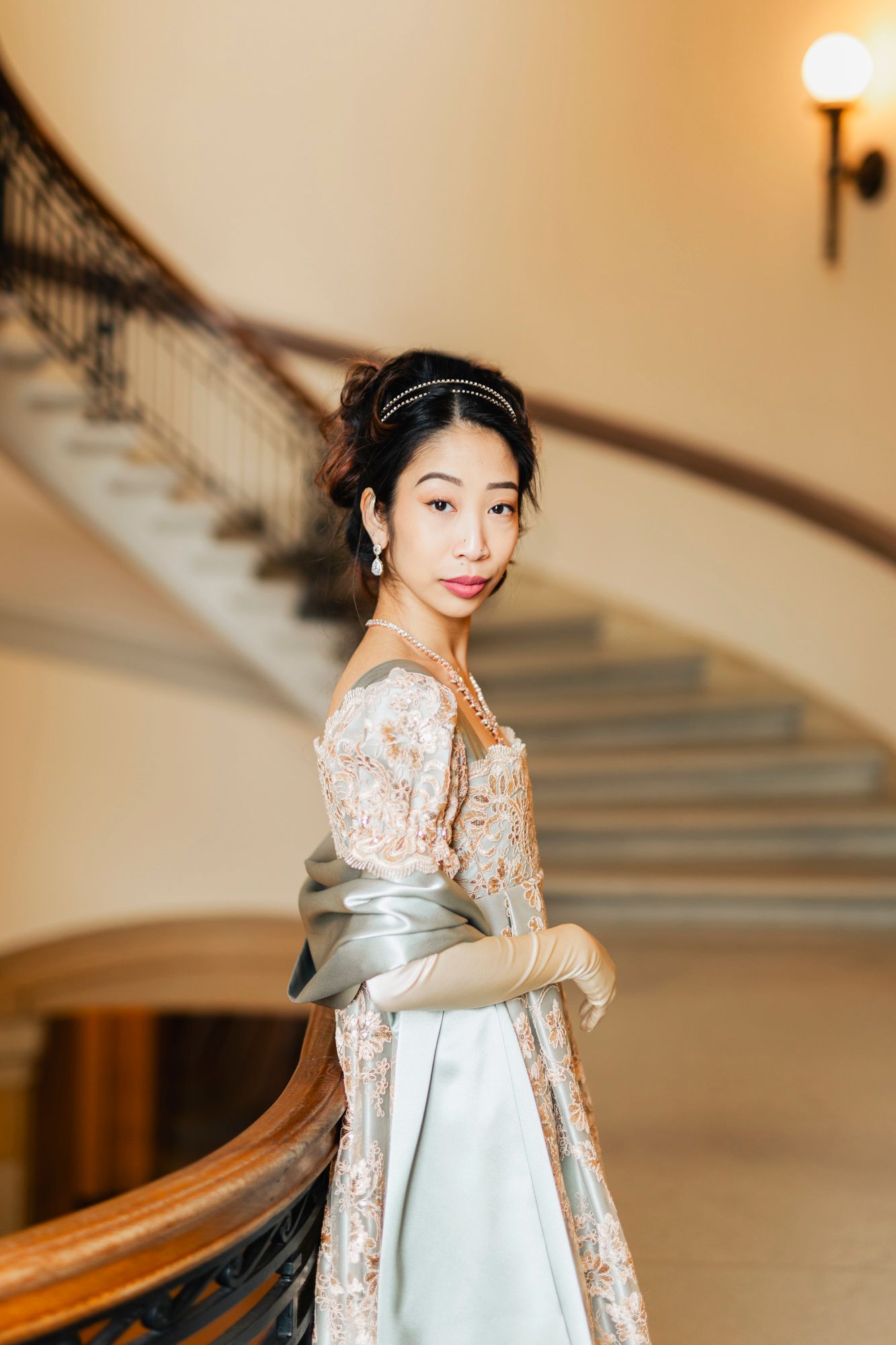Elegant portrait of person in vintage-inspired lace gown on grand staircase.