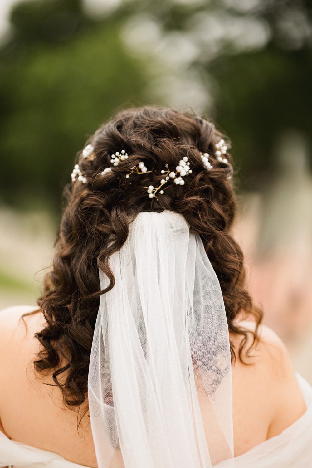 Close-up details of delicate white flower accessories adorning curled hair with a veil.