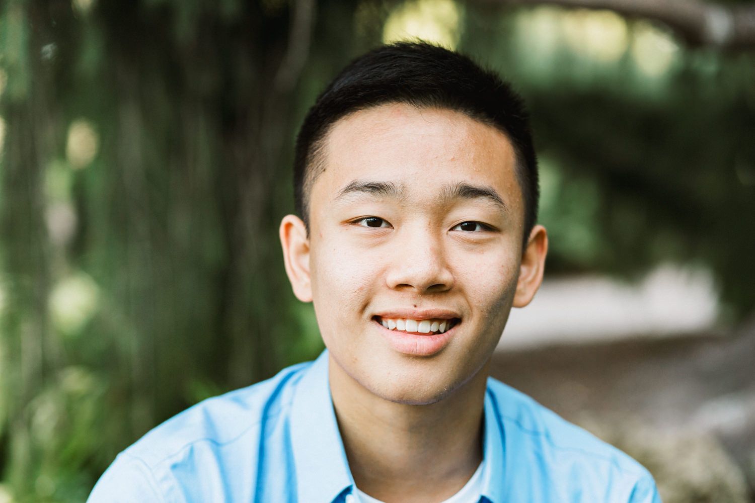 Casual outdoor portrait with light blue shirt against lush forest greenery.
