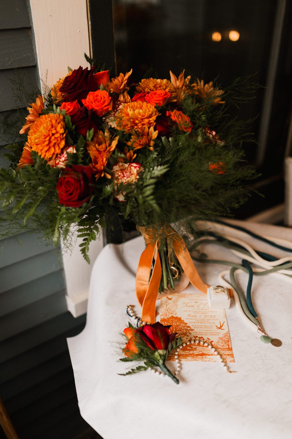 Orange and red fall floral arrangement in white vase with decorative ribbon sits on white tablecloth.