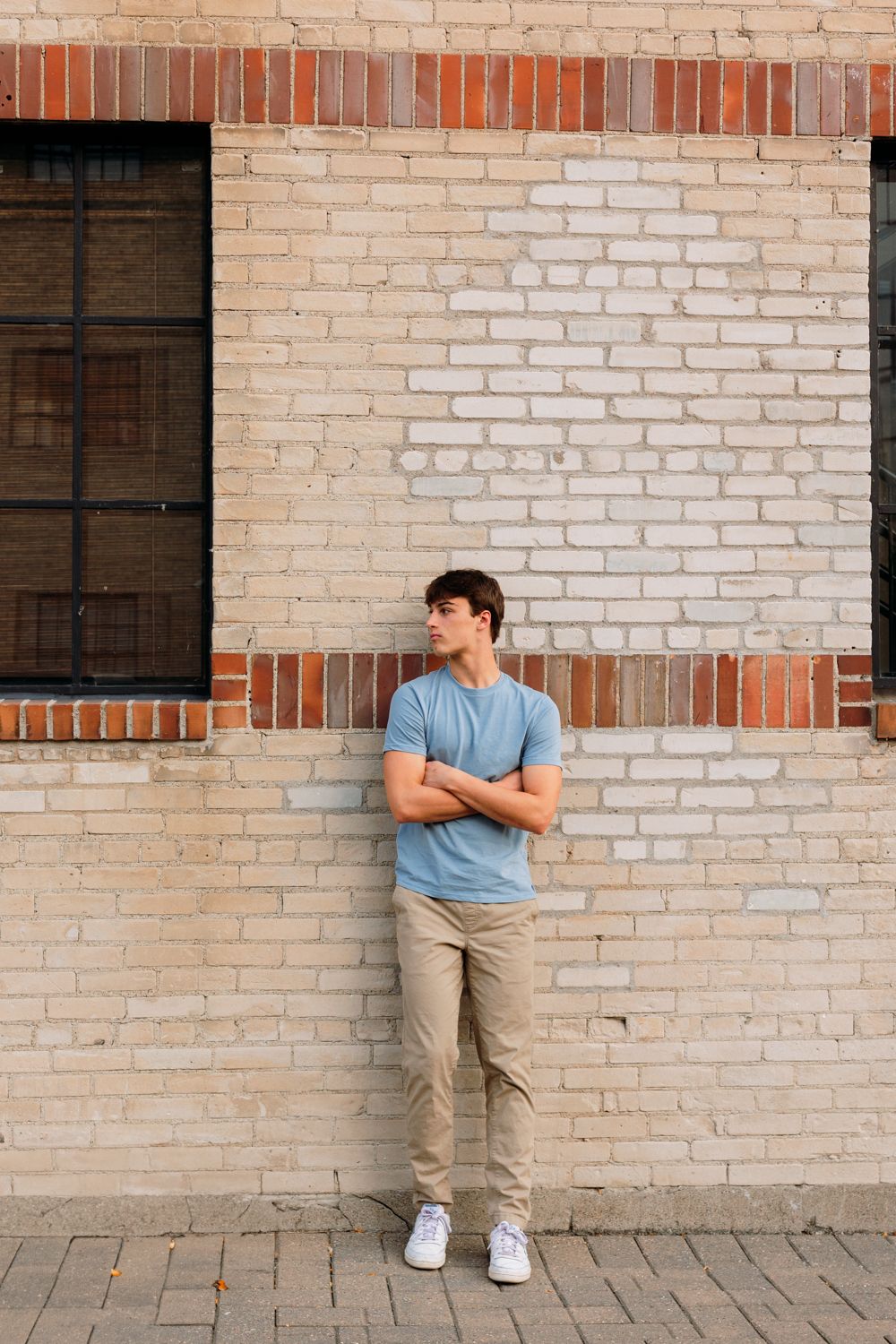 Urban fashion portraits showcasing relaxed poses against a light brick wall with industrial windows.