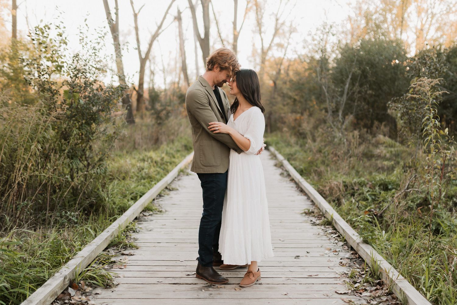 Romantic couple sharing an intimate moment on a wooden boardwalk path surrounded by lush greenery.