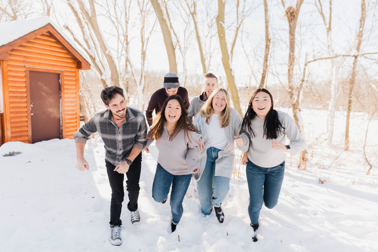 Energetic family running and playing together in a snowy winter setting with orange cabin visible.