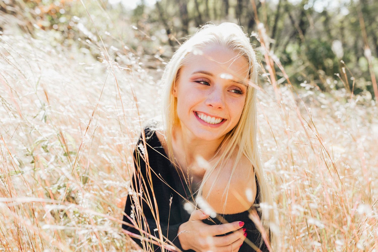 Candid outdoor portrait showing joyful expression while sitting in a sunny field.