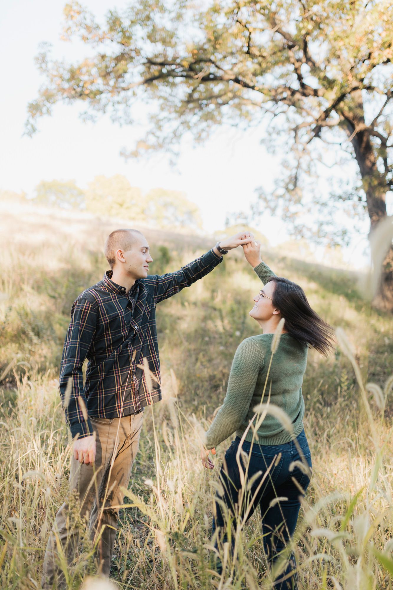 A couple dances together in a sunlit meadow with tall grass and trees in the background.