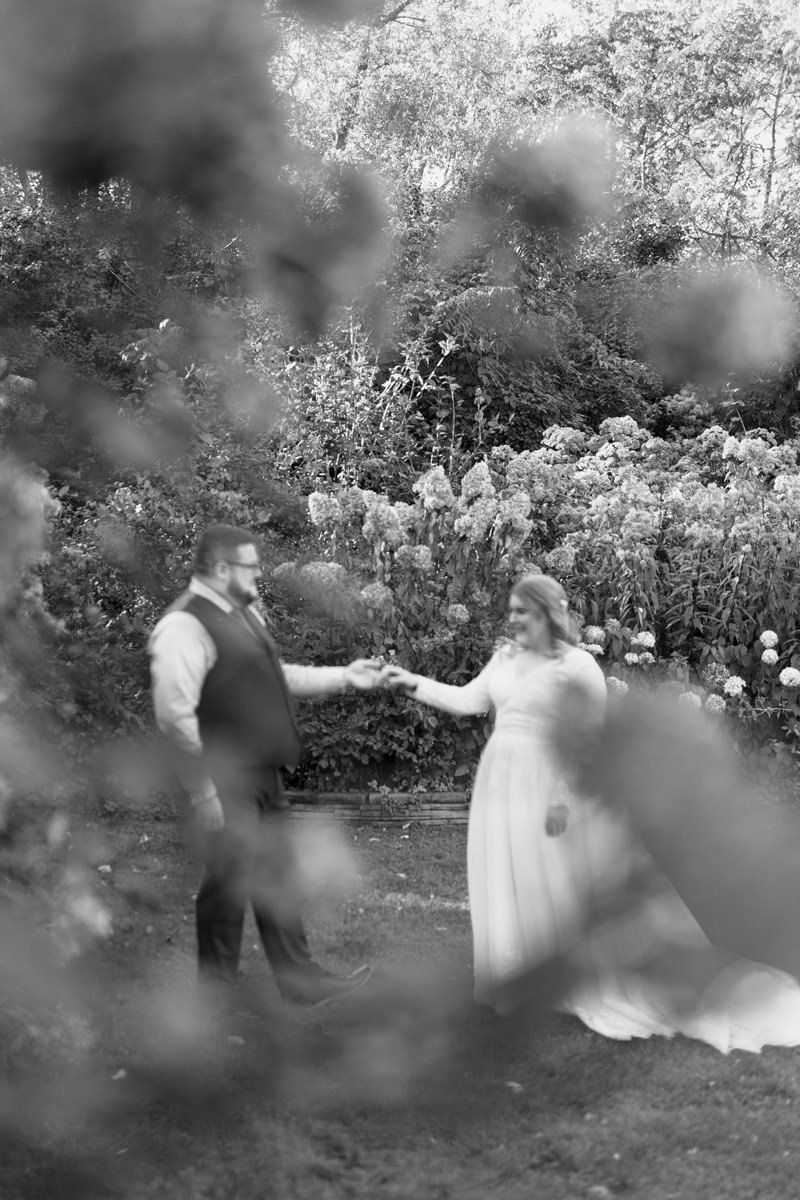 A romantic couple dances together in a garden setting, creating a dreamy black and white moment.