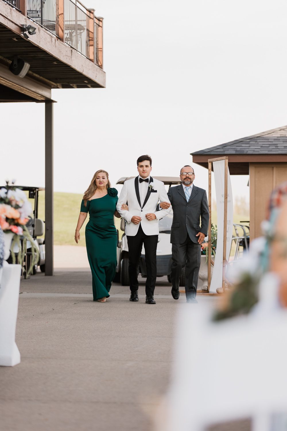Wedding processional on a covered walkway with attendants in formal attire walking together.