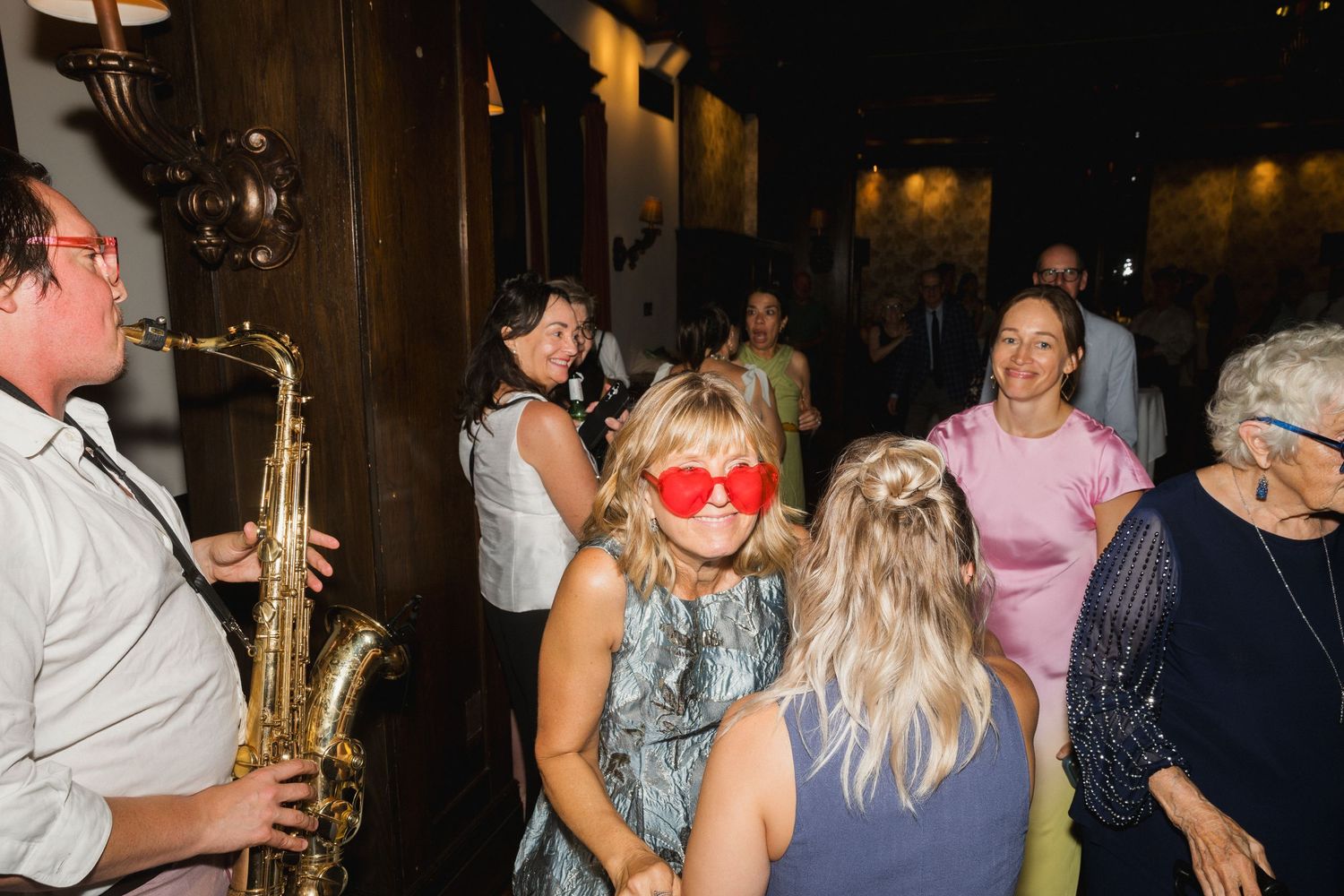 Lively wedding reception dance floor with saxophone player and guests wearing fun red sunglasses.