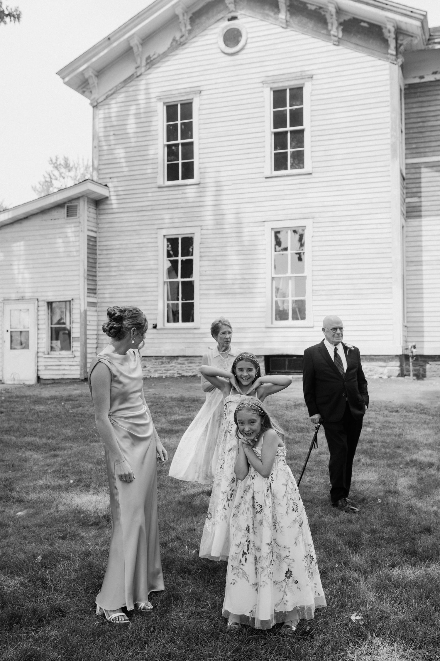 Black and white wedding photo of bridesmaids and flower girls laughing outside a white historic building.