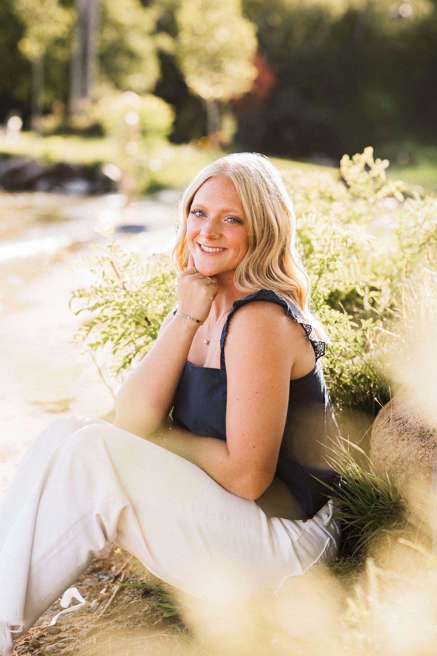 Person in black dress reclining on white blanket in sunny garden setting with soft bokeh background.