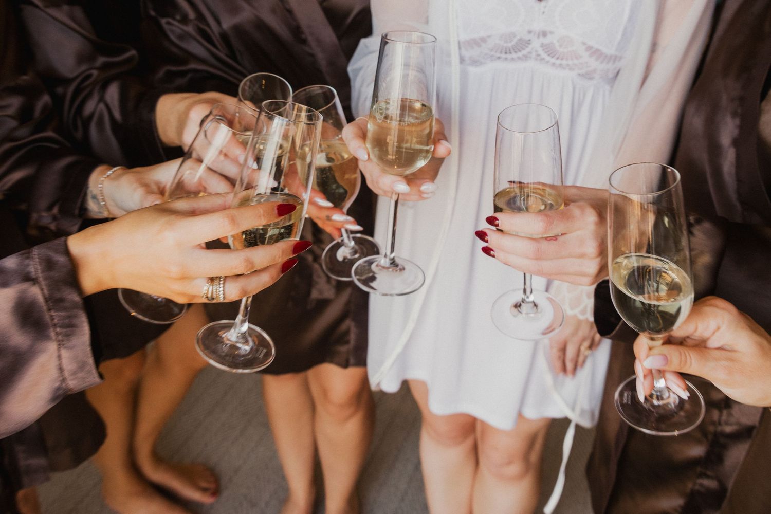 Group of women in matching robes clinking champagne glasses together during a bridal party celebration.