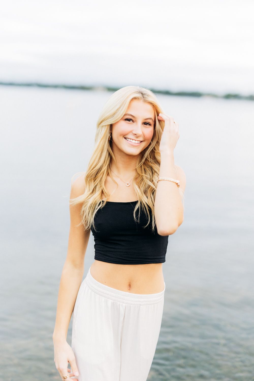 Woman in black crop top and white skirt smiling on the beach at sunset.