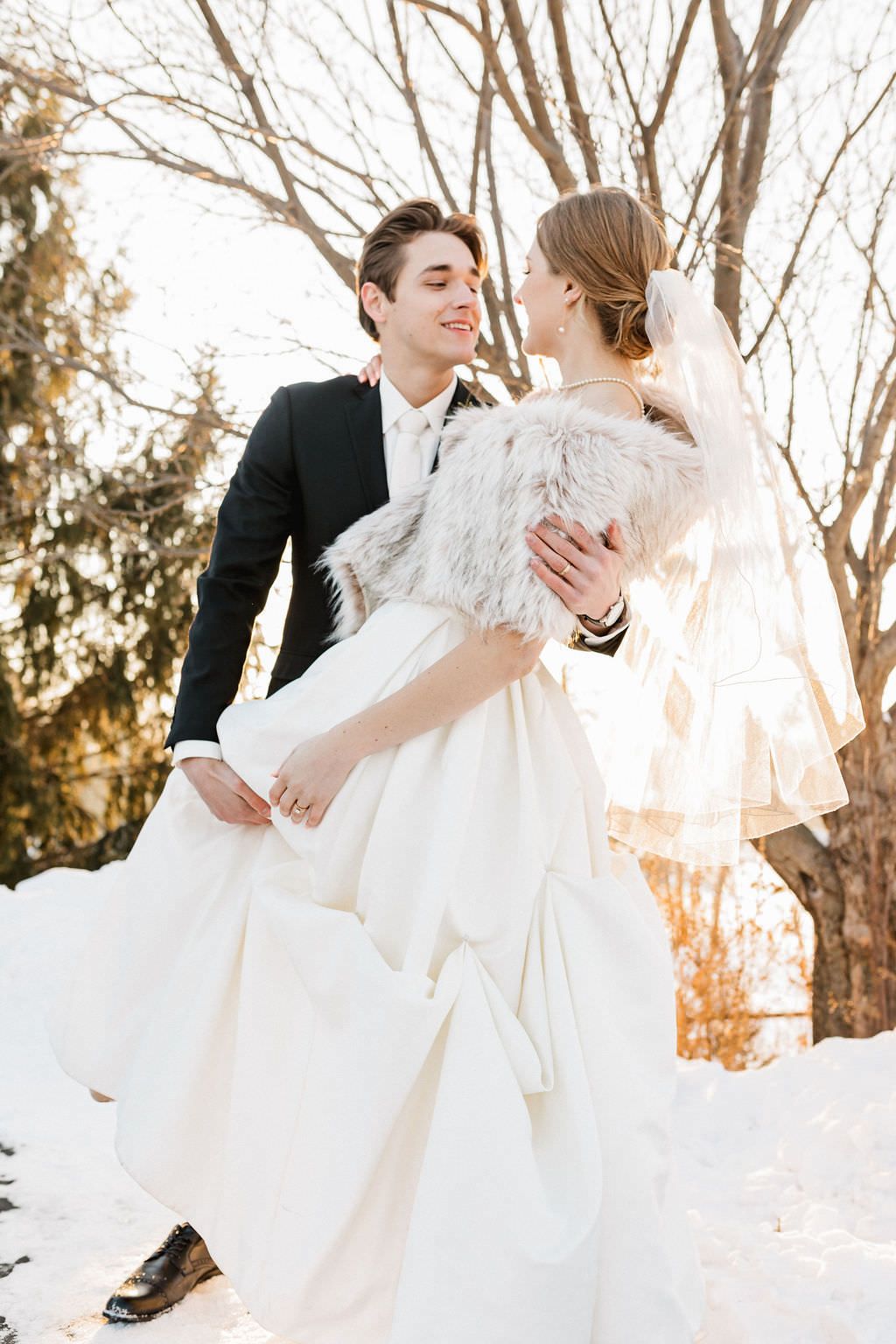 A couple takes romantic wedding photos in a snowy winter landscape at sunset.