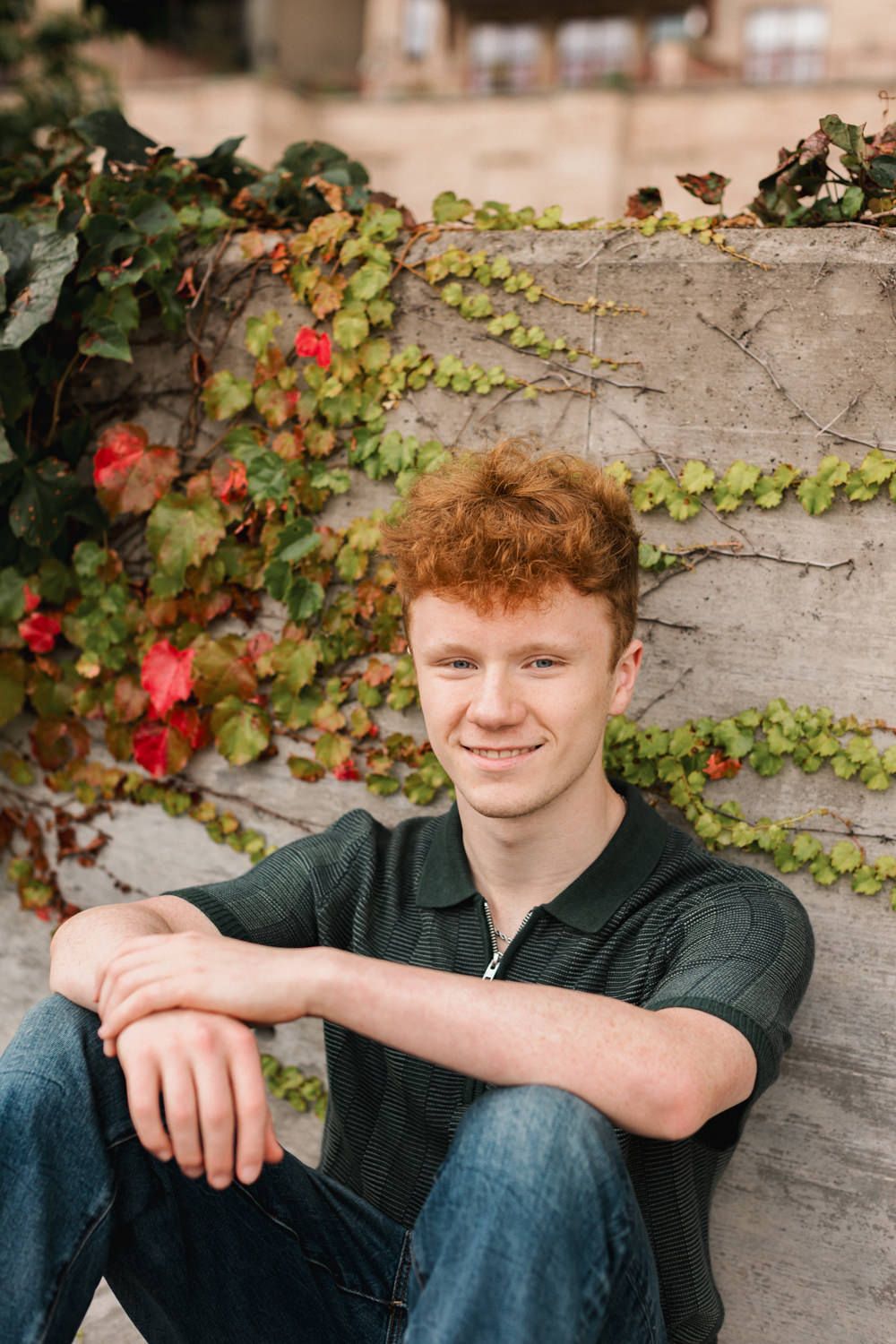 Casual portrait by concrete wall with red flowering vines and greenery.