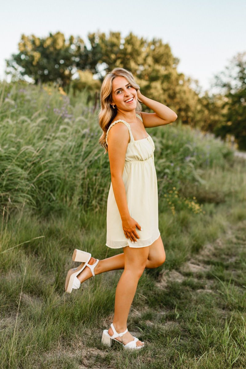 Woman in light summer dress posing playfully in grassy field wearing platform sandals.
