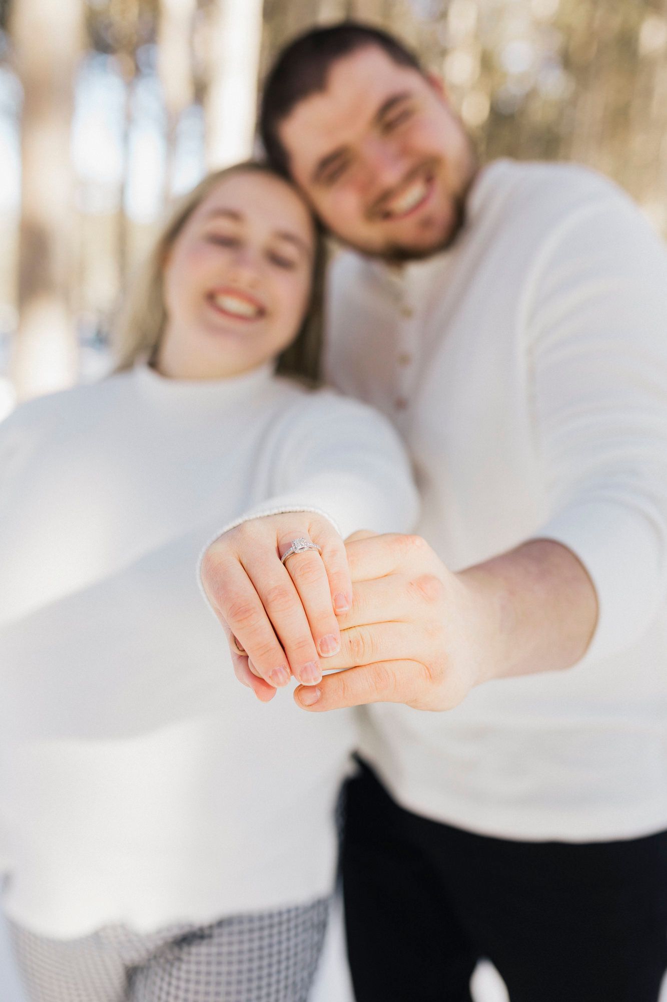 Close-up of hands showing off an engagement ring against a soft blurred background.