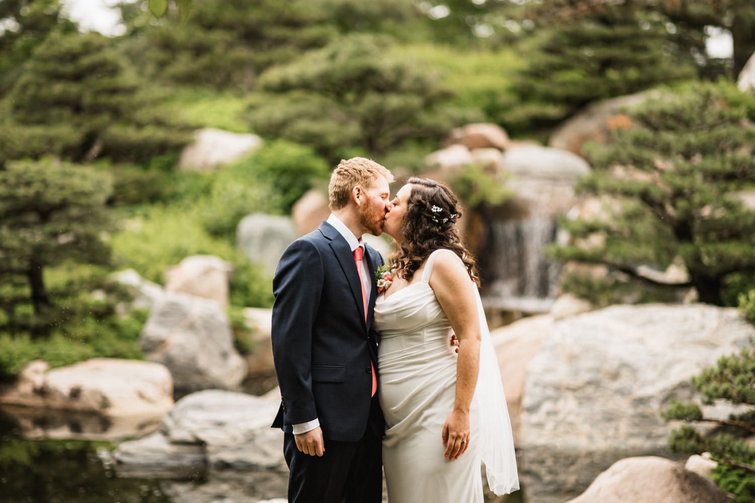 A romantic wedding moment between newlyweds in an outdoor garden with stone features.