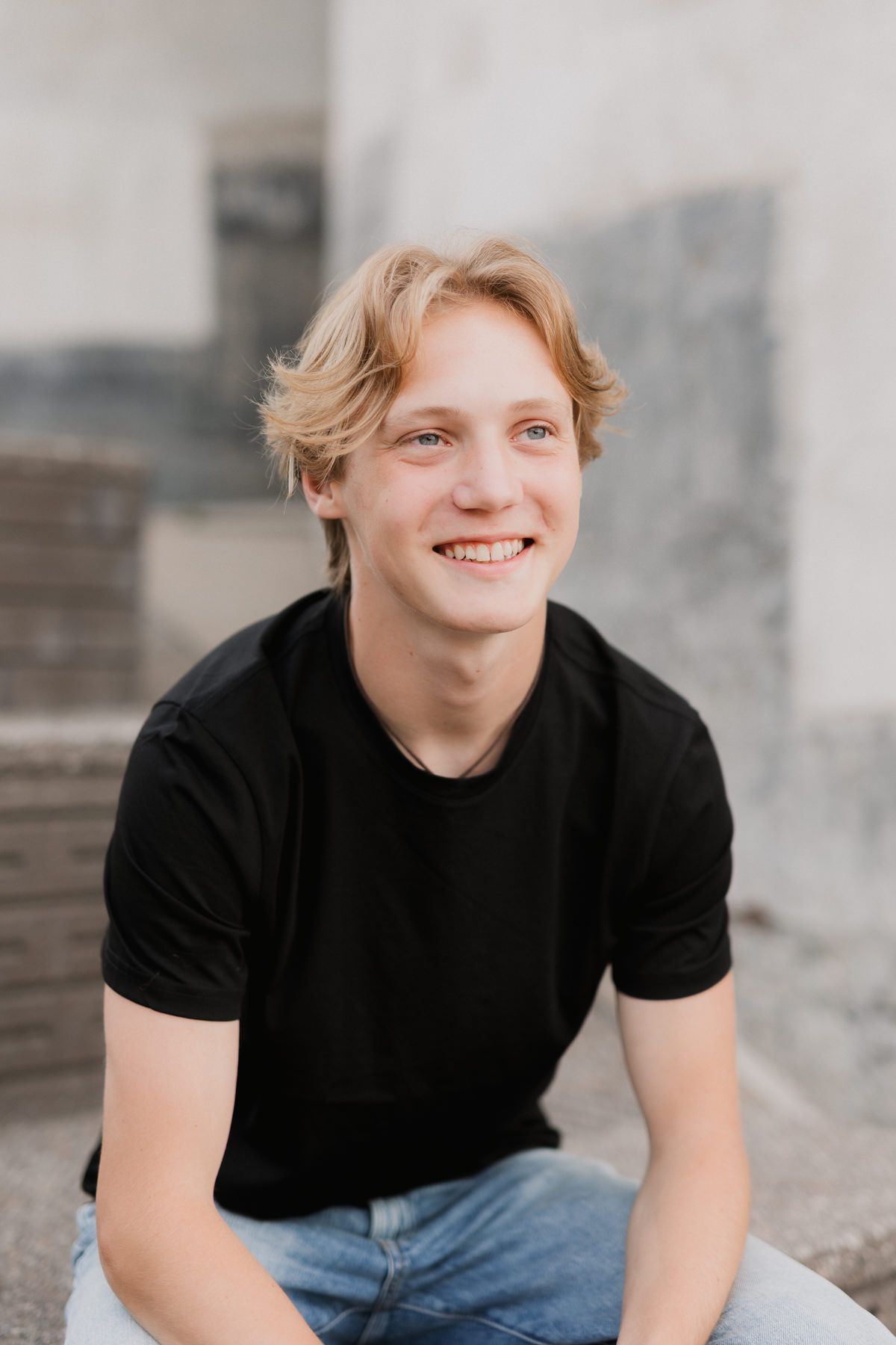 Smiling young blond man in black t-shirt and jeans sitting outdoors.