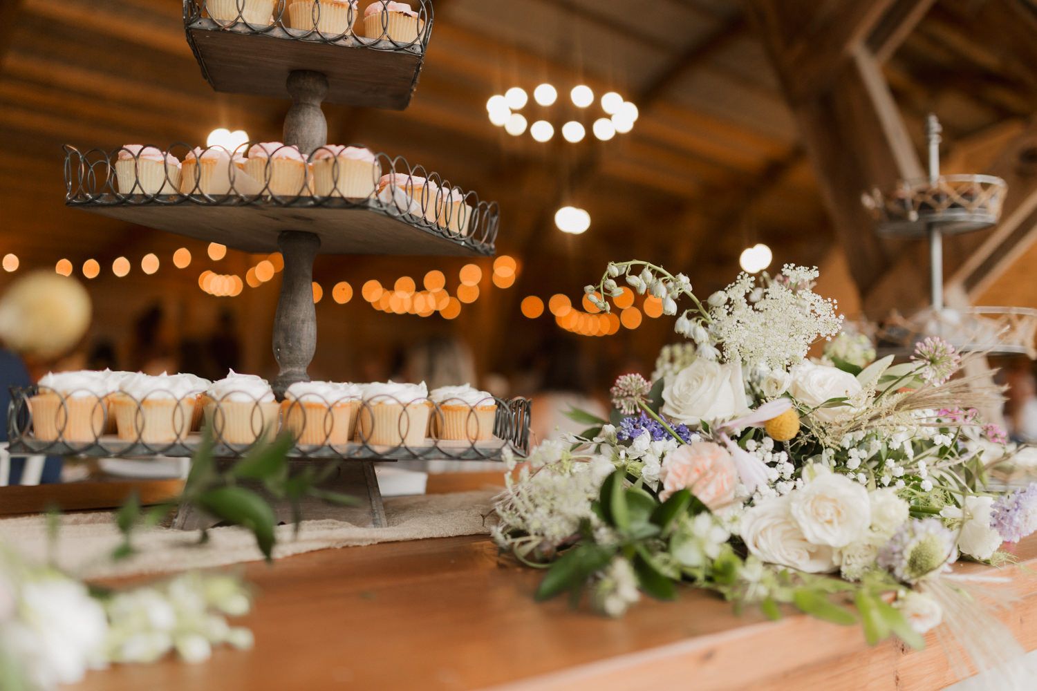 Elegant wedding reception decor with white floral arrangements and warm lighting in a rustic barn venue.