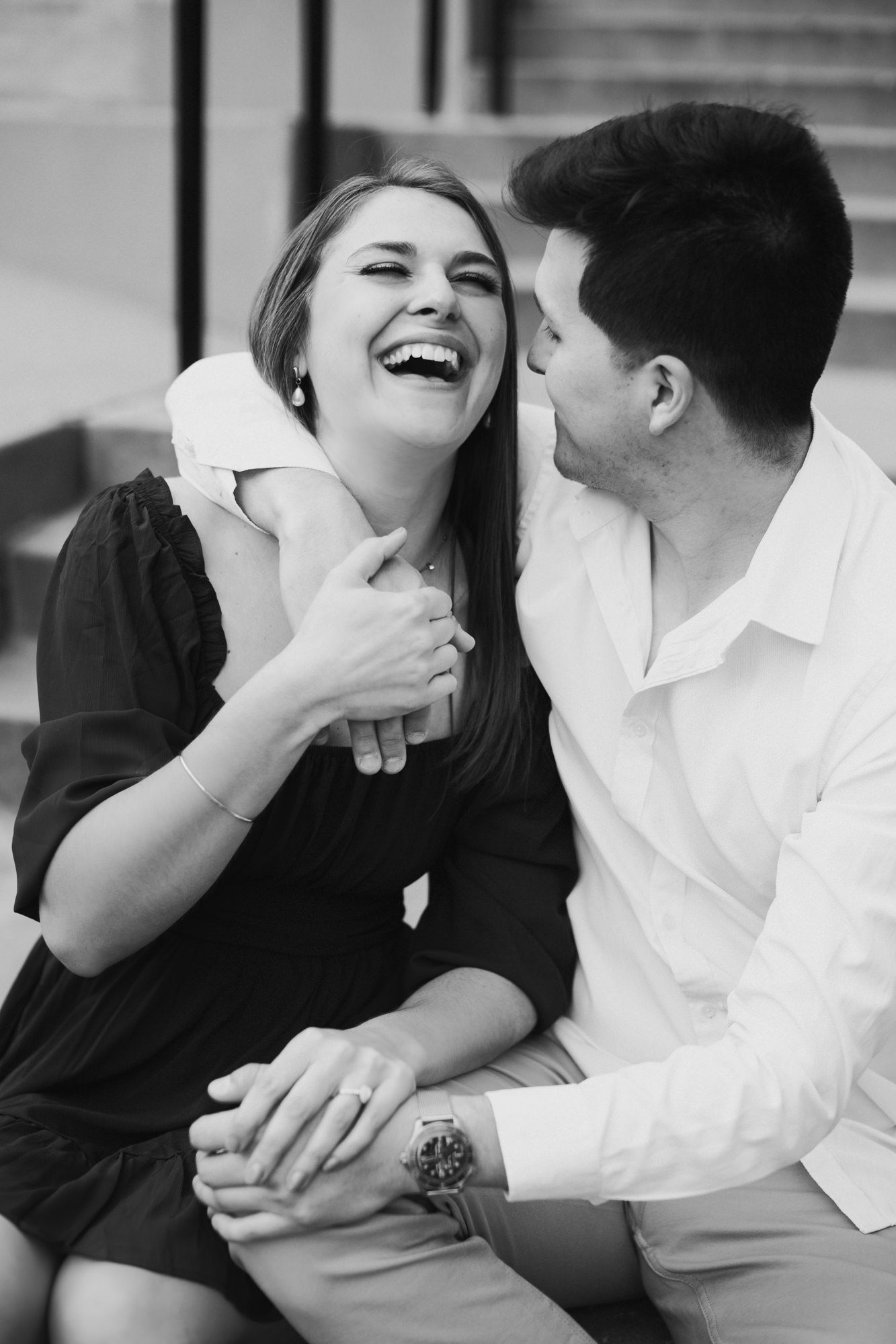 Black and white photo of a laughing woman and smiling man sitting together holding hands.