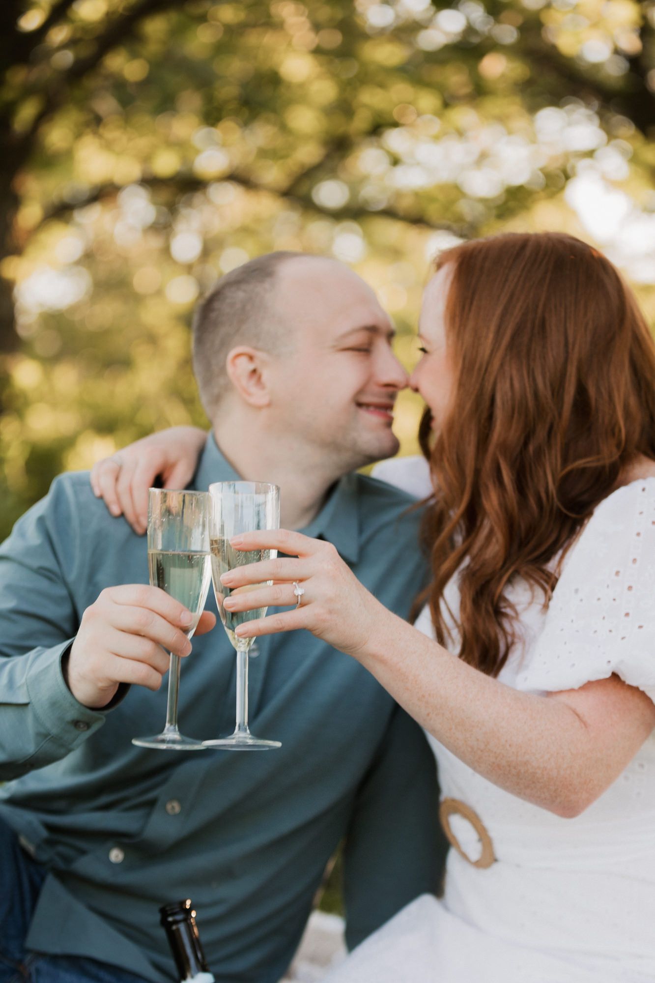 Couple clinking champagne glasses and sharing a romantic moment outdoors during an engagement celebration.