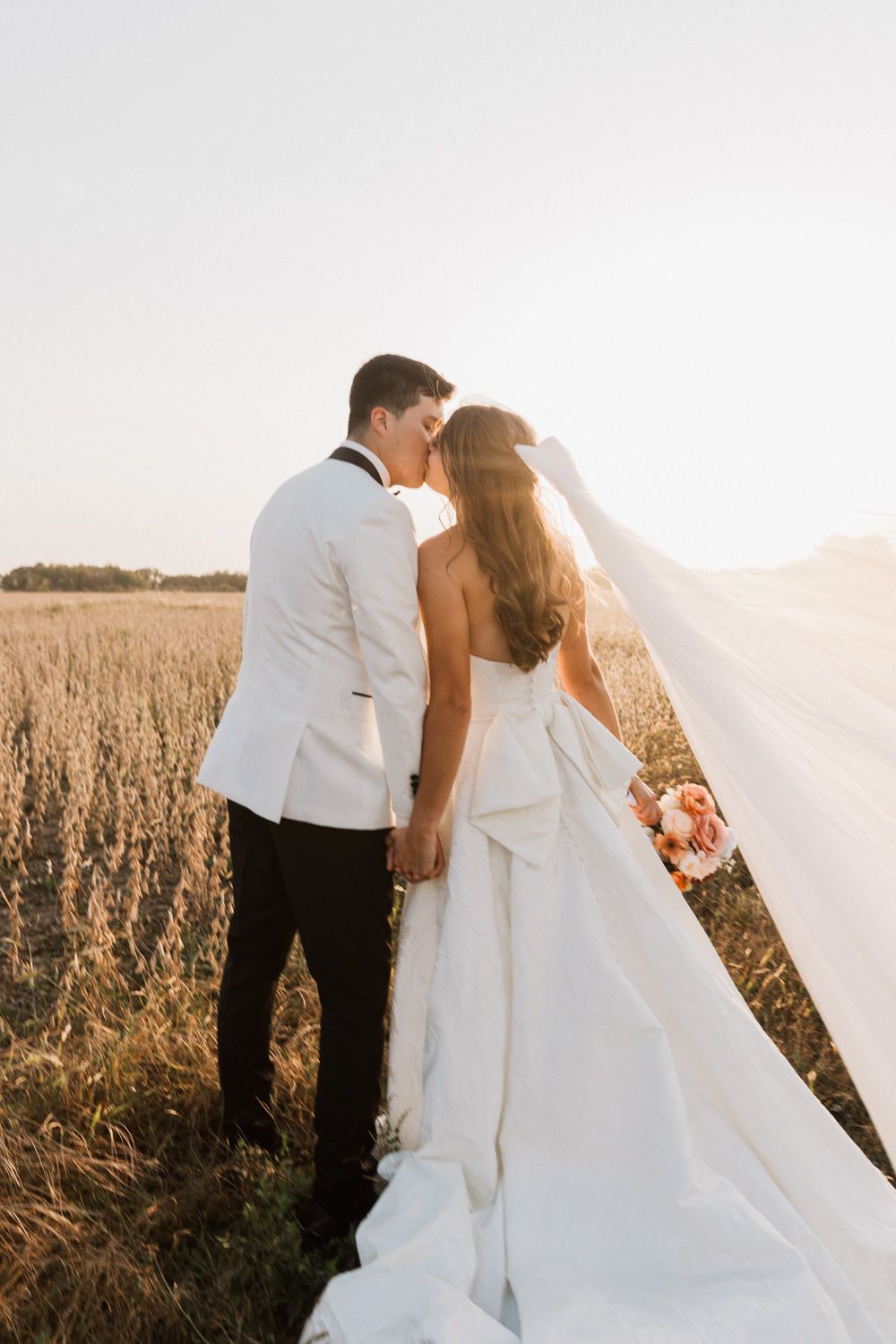 A romantic wedding couple embraces in a golden wheat field at sunset creating a dreamy silhouette.
