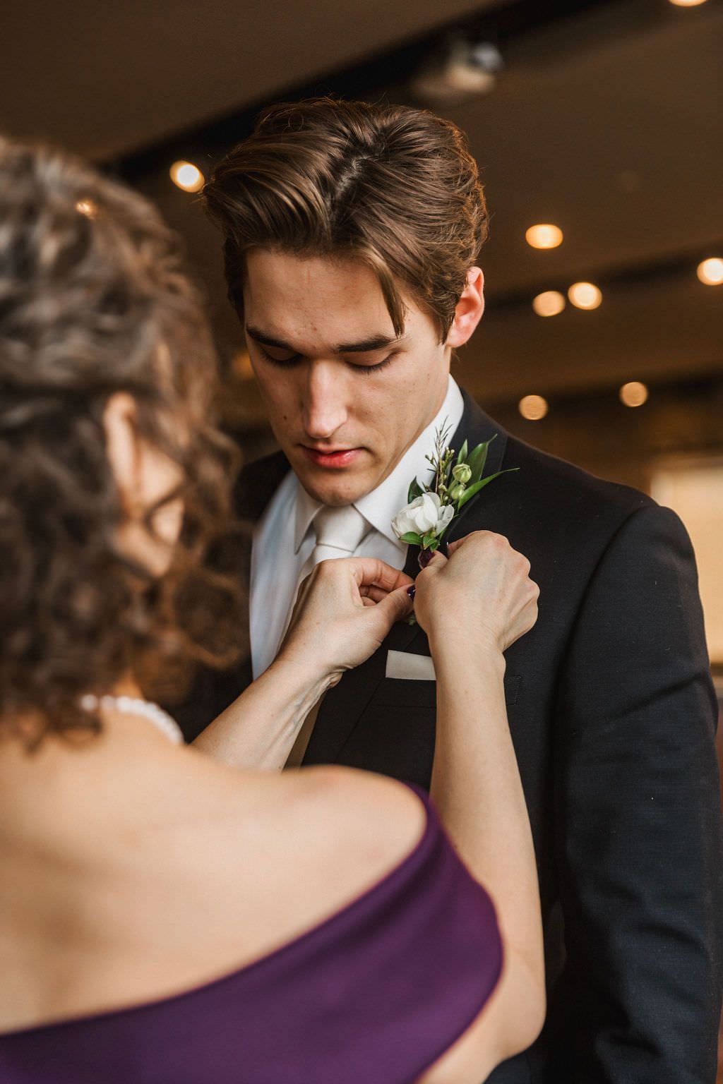 Intimate wedding moment captured in warm indoor lighting with floral boutonniere detail.