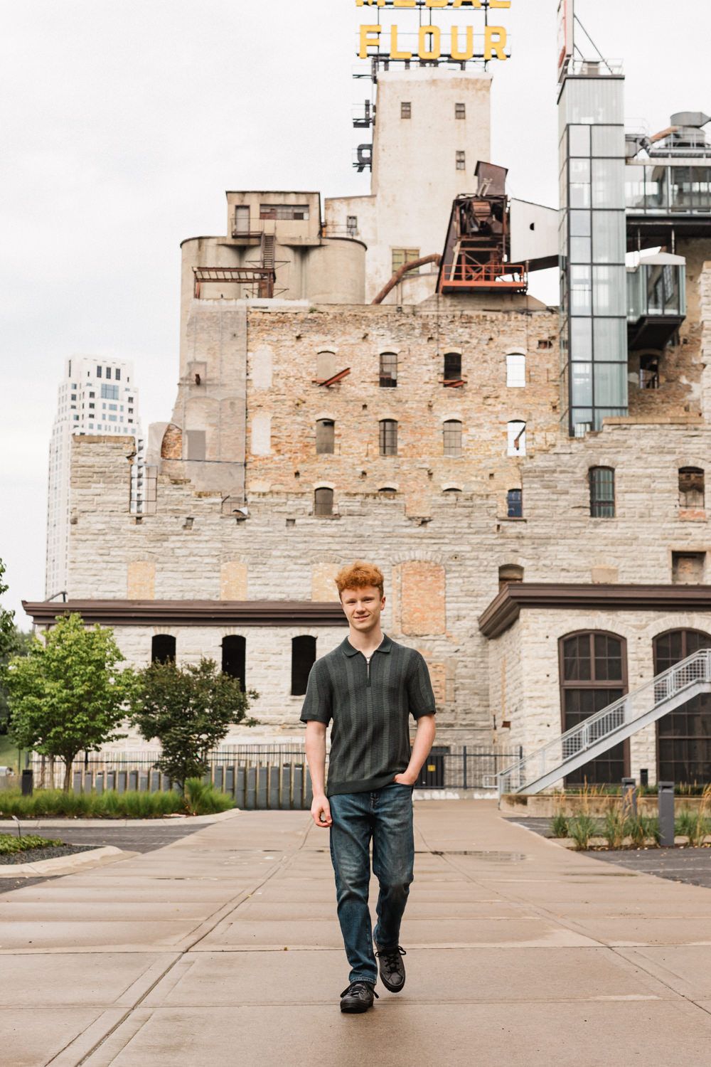 Man walking past historic brick walls in an urban plaza with downtown buildings visible in background.
