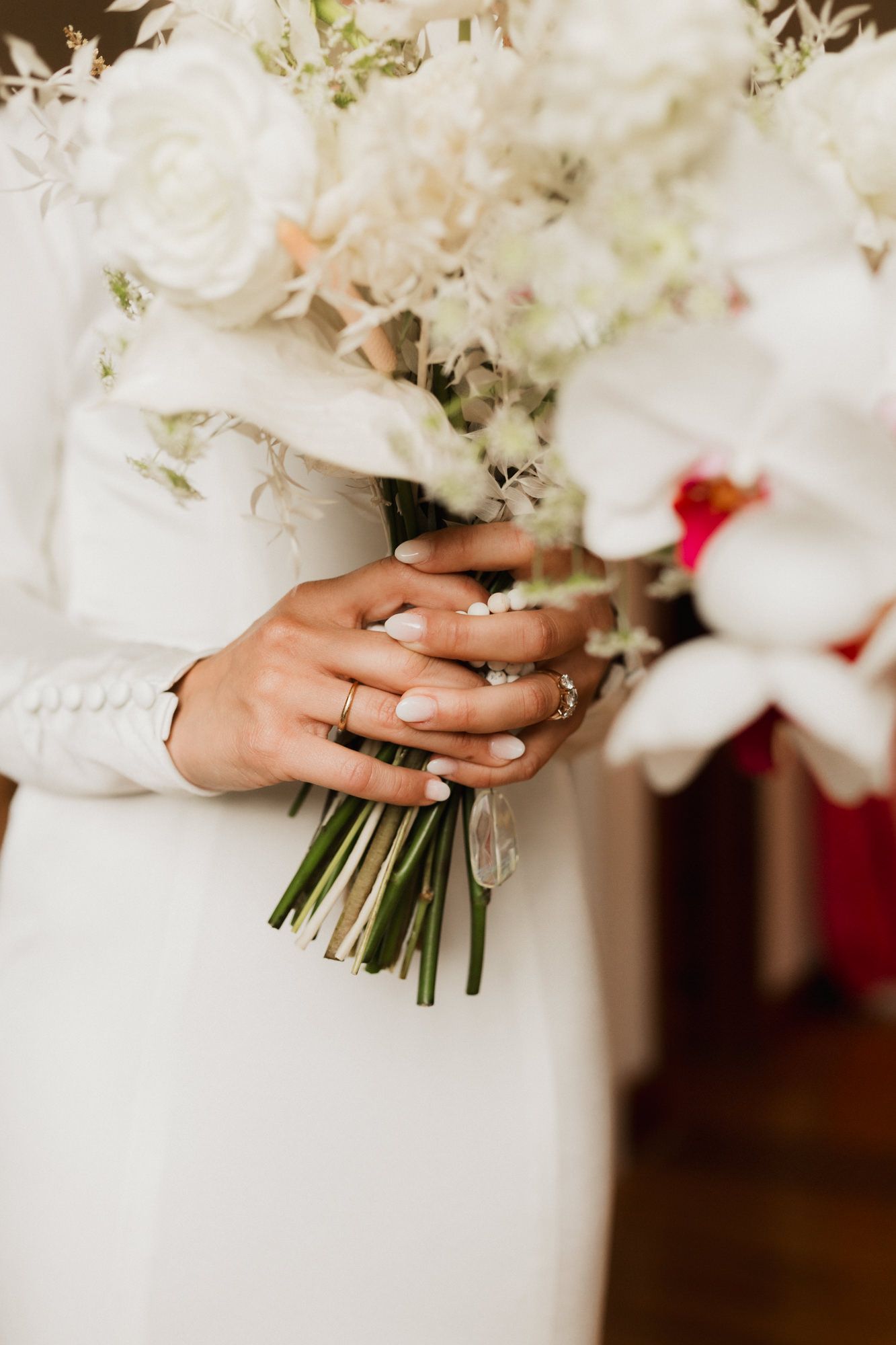 Bride holding a lush white wedding bouquet with roses and orchids, wearing a diamond engagement ring.