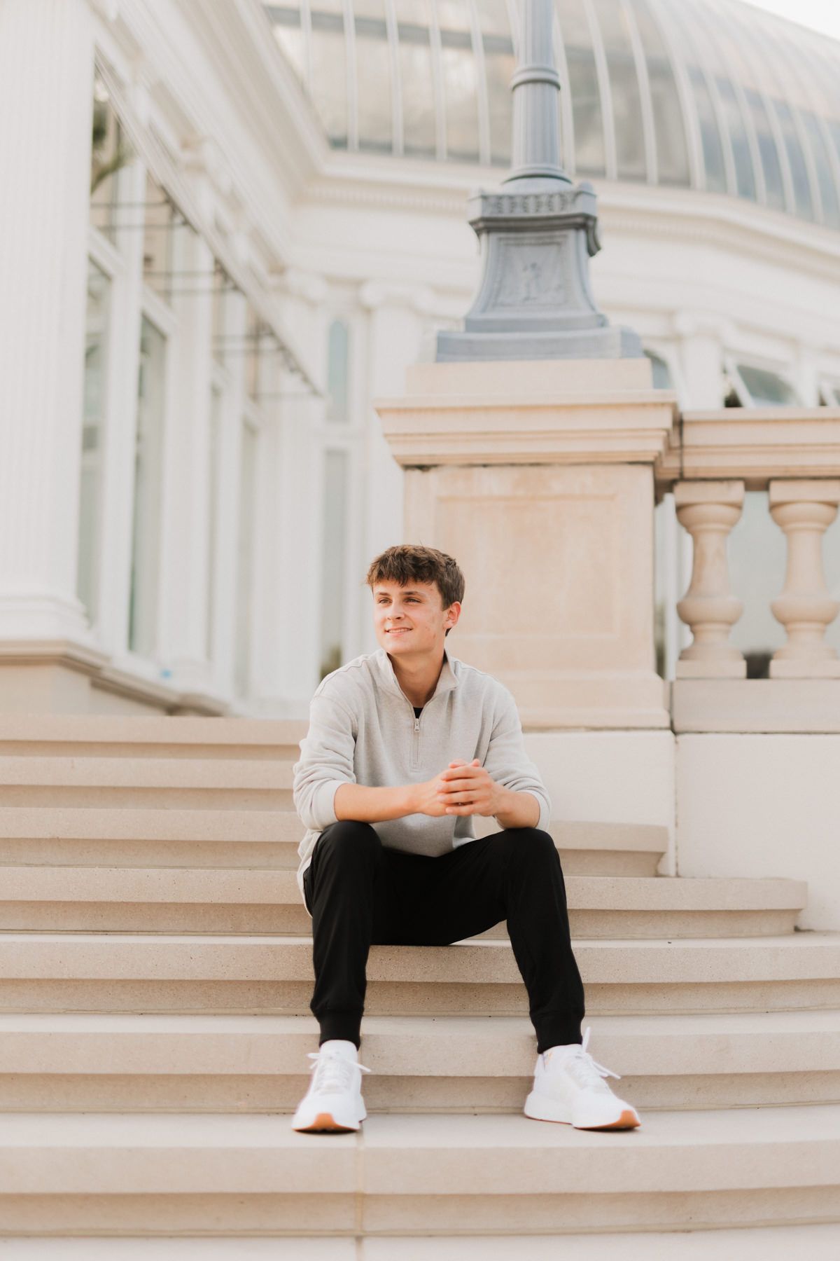 Young man in gray sweatshirt sitting on white stone steps outside elegant building.
