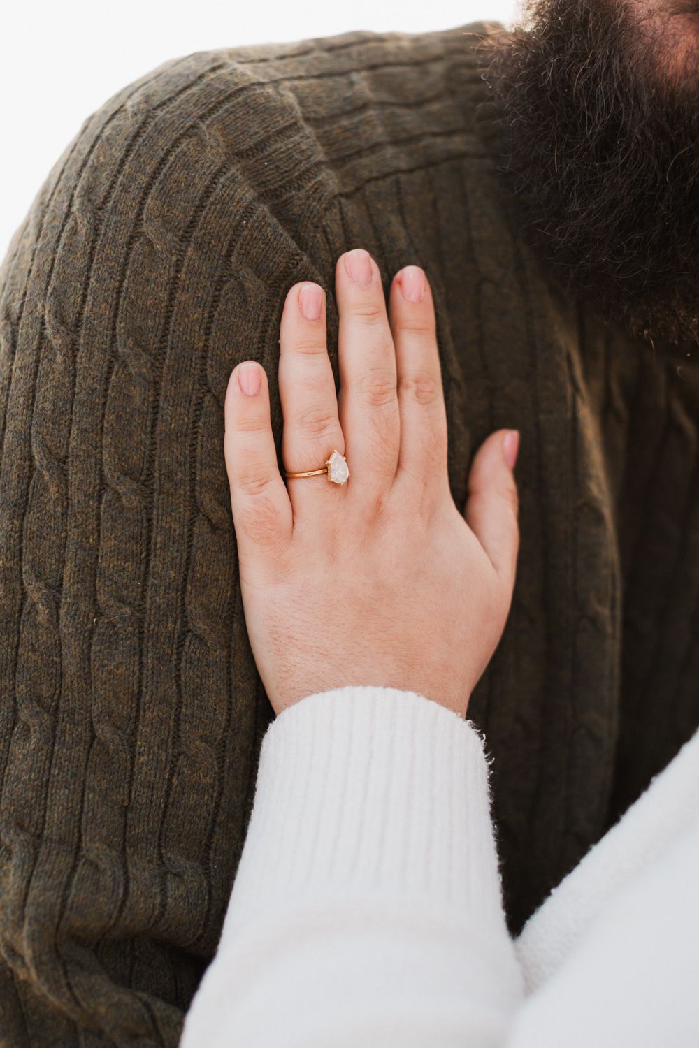 Close up of hand with engagement ring resting on brown knit sweater.