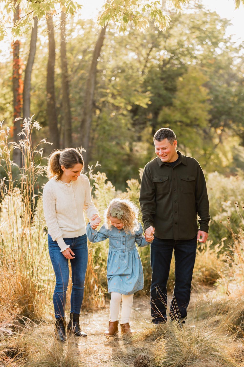 Family walking together through tall golden grass in a sun-drenched outdoor setting during autumn.