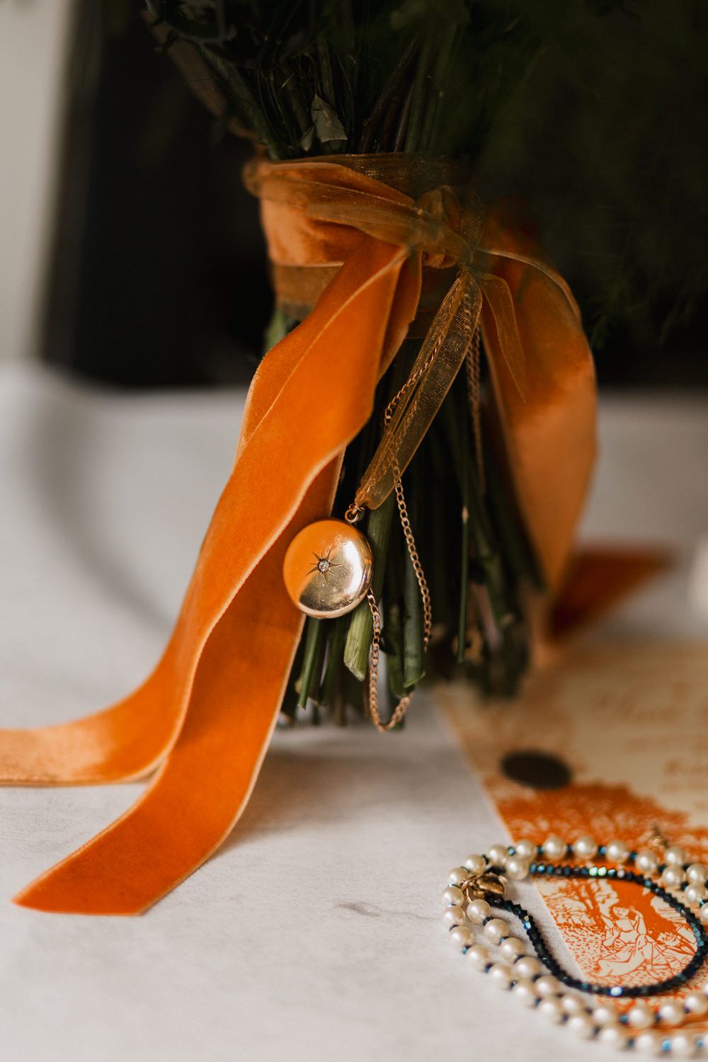 Close-up view of an orange velvet ribbon with gold accents and pearls on a light surface.