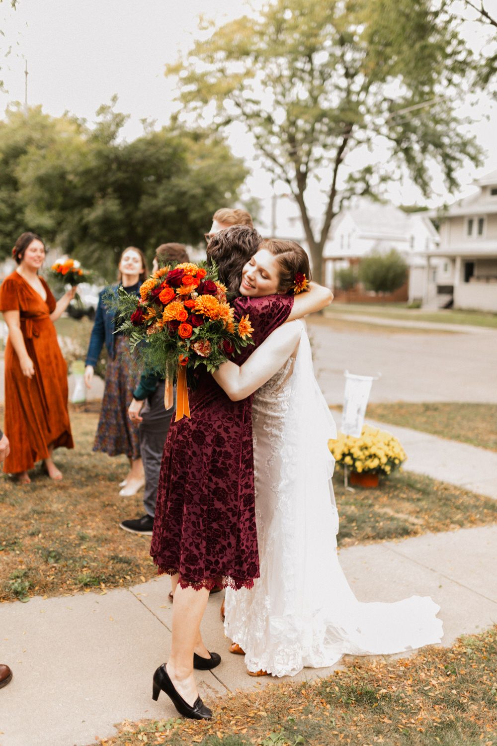 Candid moments at a fall wedding showing joyful interactions between people in burgundy and white dresses on a sidewalk.