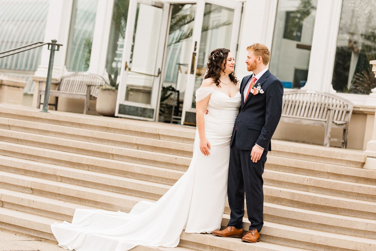 A bride and groom share a tender moment on stone steps outside a modern building on their wedding day.