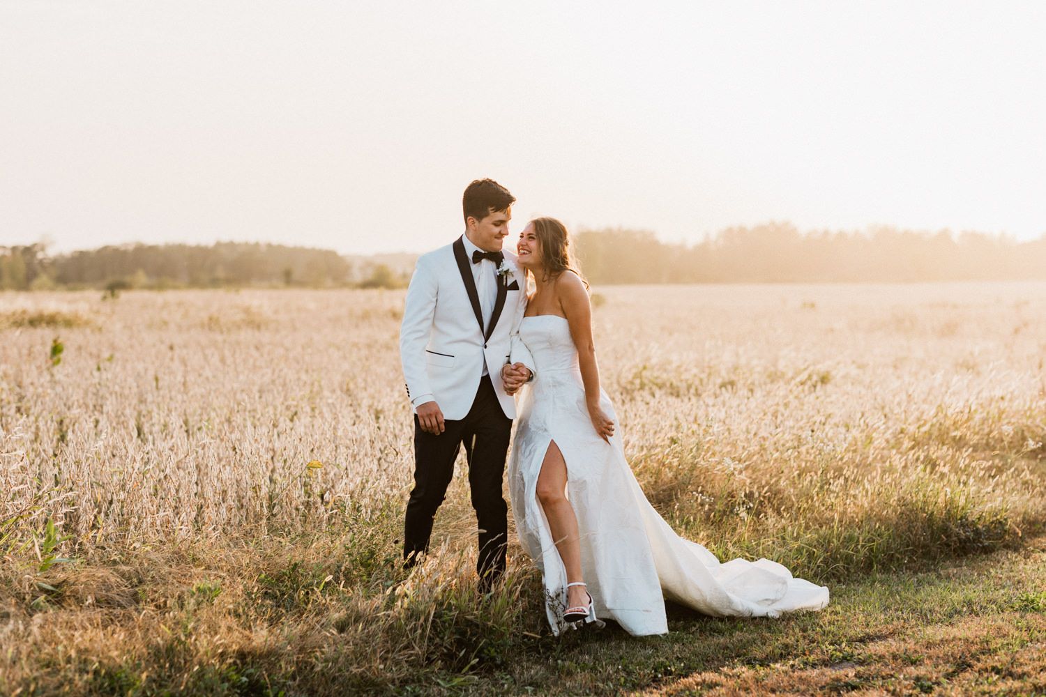 A couple shares an intimate moment in formal wear while standing in a golden wheat field at sunset.