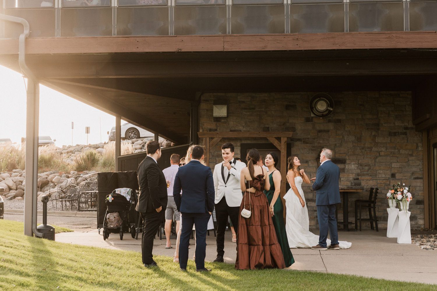 Wedding party members gather under an outdoor overhang during sunset.