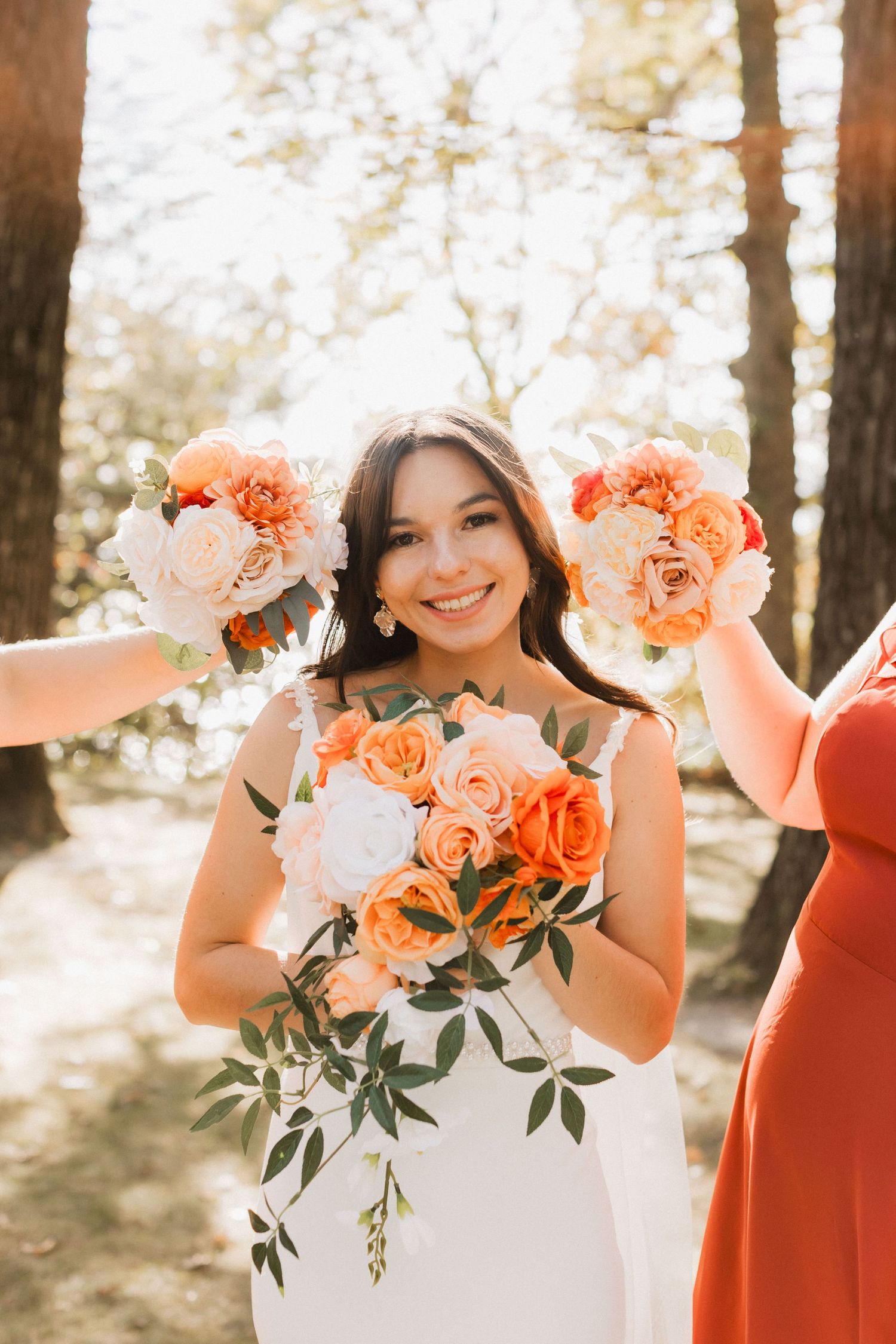 Wedding party poses with peach roses in a sunlit forest setting.