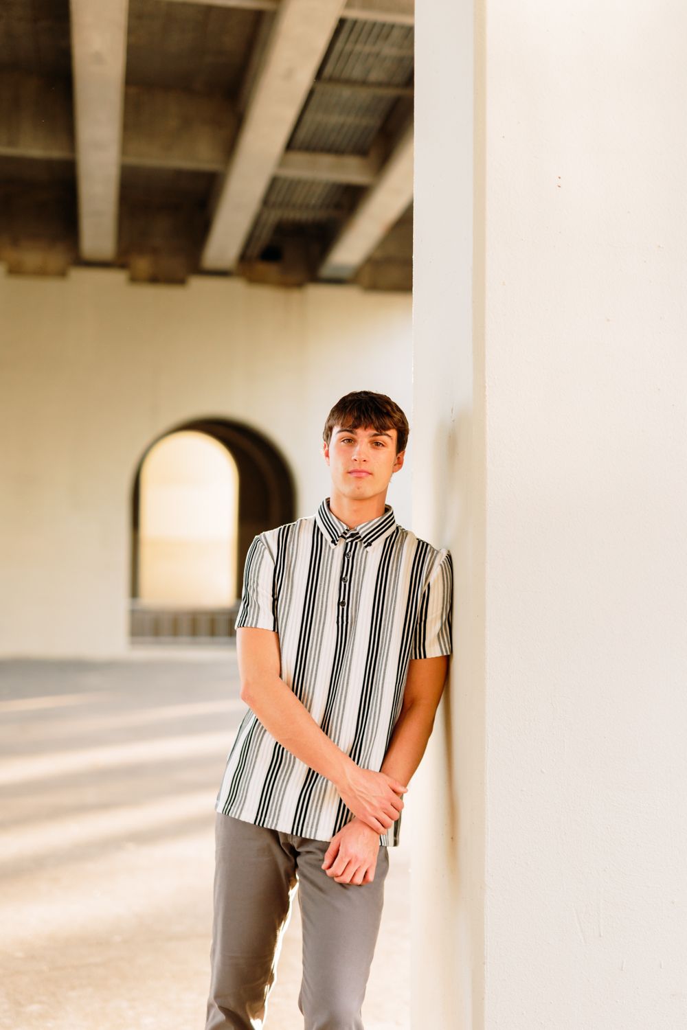 A trendy striped button-down shirt is worn in a minimalist architectural setting with white columns.