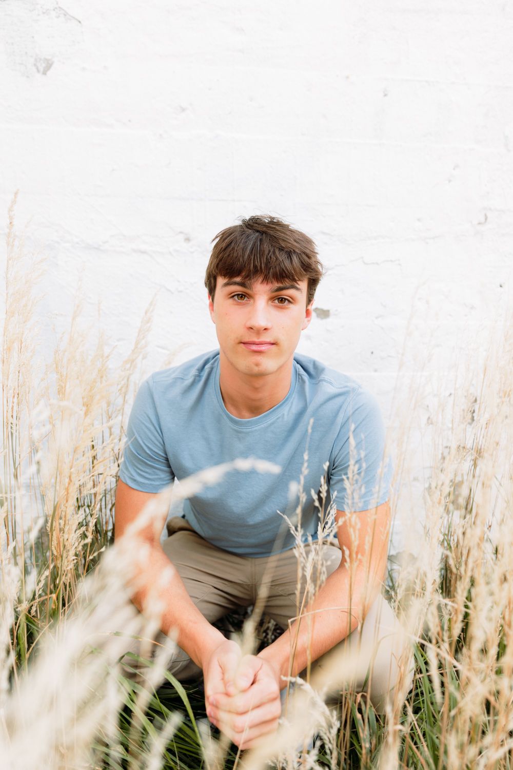 Person in light blue shirt sitting among tall grass during outdoor photoshoot.
