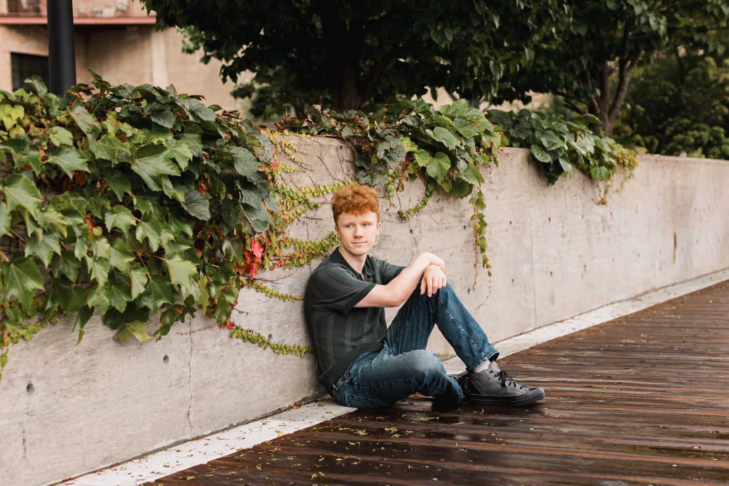 Person sitting on wooden bench with ivy-covered wall in background.