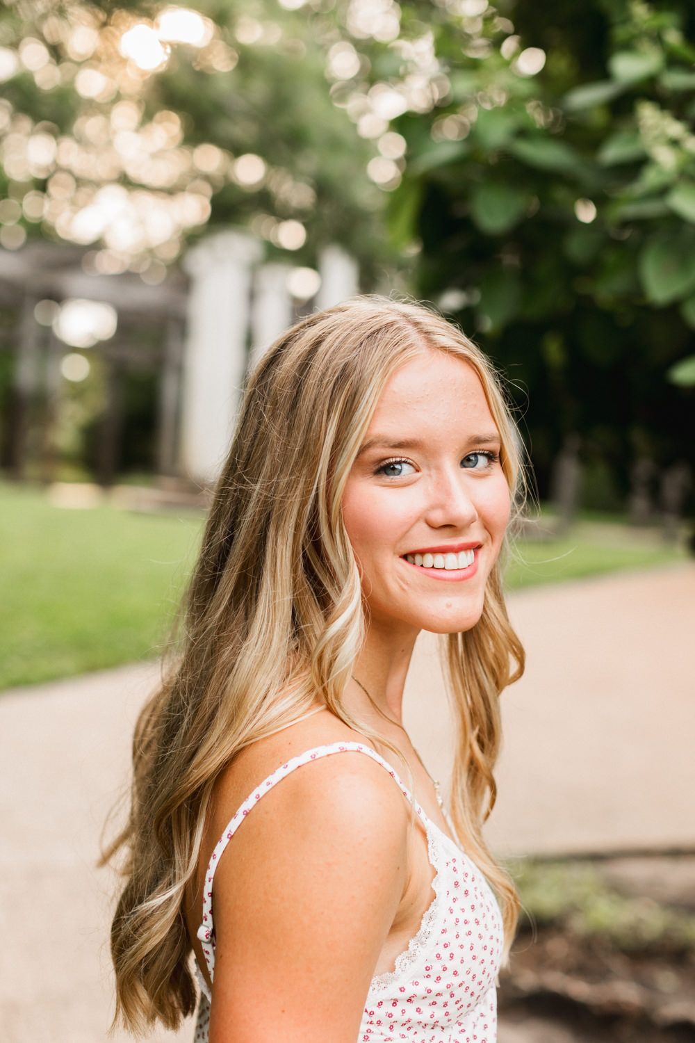 A glowing golden hour portrait on a garden path with soft bokeh lighting and lush greenery in the background.