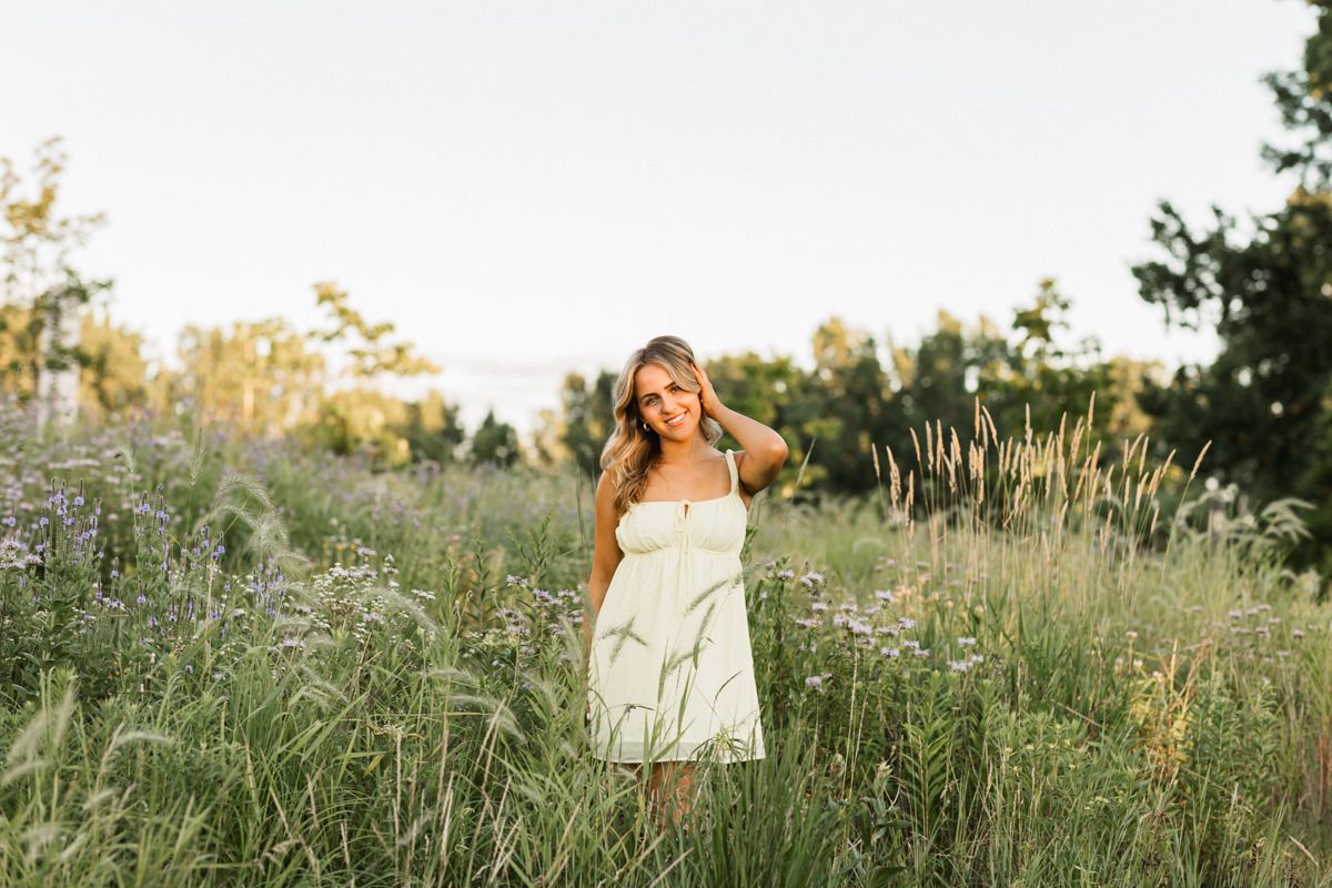 A white sundress flows in a golden meadow filled with tall grasses and wildflowers at sunset.