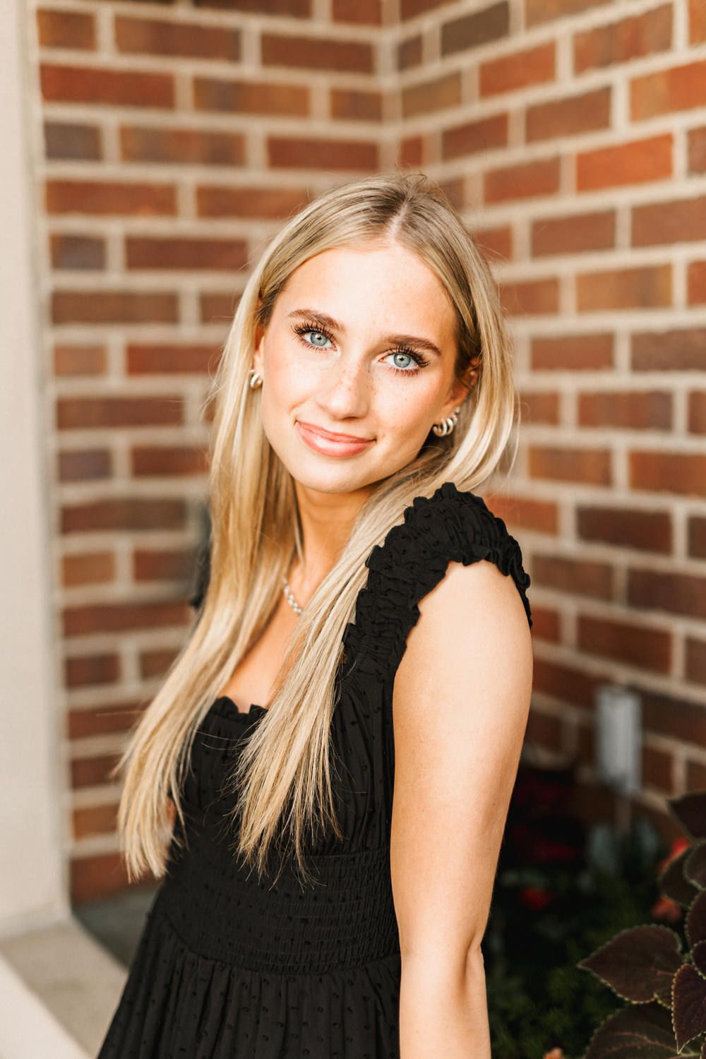 Close-up portrait against brick wall background showcasing black summer dress and delicate jewelry.